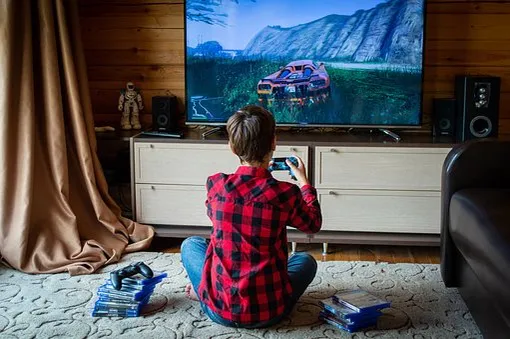 мальчик в клетчатой красной рубашке сидит спиной к зрителю и играет в компьютерную игру