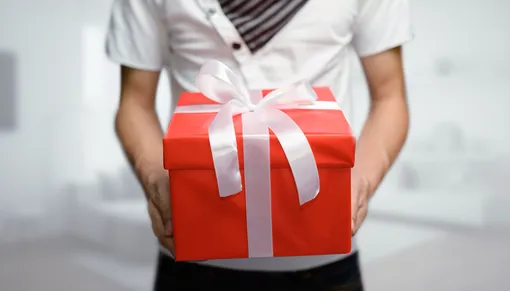 юноша держит в руках красную коробку с подарком