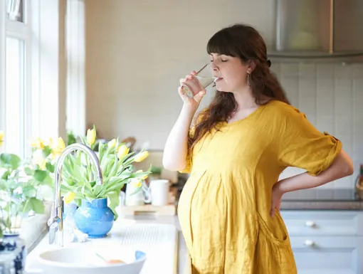 беременная женщина пьет на кухне воду