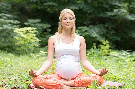 беременная женщина на природе сидит в позе лотоса и медитирует