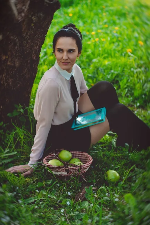 Девушка под деревом с книгой и корзинкой яблок