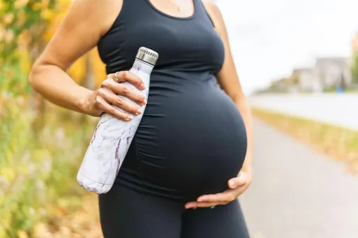 Беременная поддерживает живот и держит бутылку с напитком