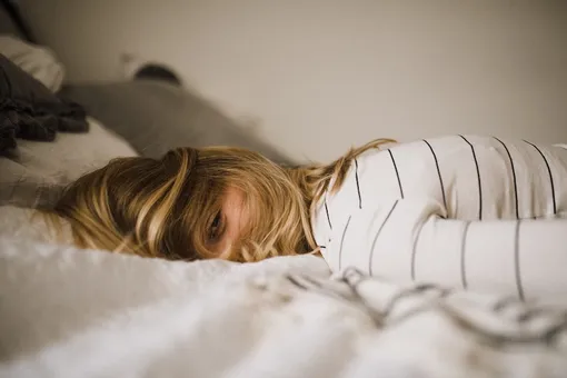 Девушка в полосатом свитере лежит с открытым глазом