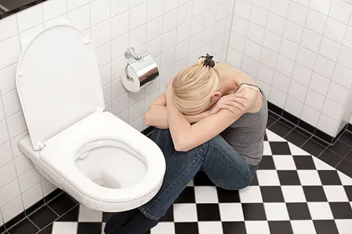 женщина в туалете сидит на полу, обняв колени и опустив голову
