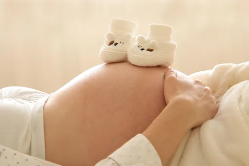 на животе беременной женщины стоят пинетки