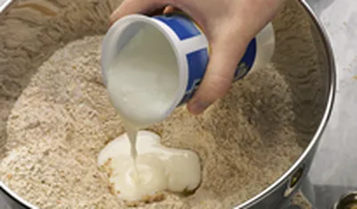 Сделайте в центре углубление и влейте пахту (кефир). Смешайте ложкой, добавляя молоко. Вымесите гладкое тесто руками.