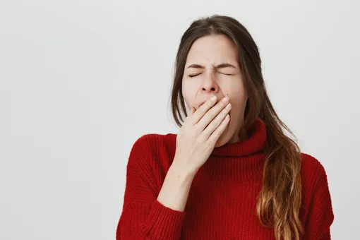 Девушка зевает, что повышает уровень глюкозы в крови