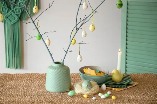 Минималистический вариант деревца: керамическая вазочка, пара раскрашенных веток и несколько миниатюрных украшений в виде пасхальных яиц.