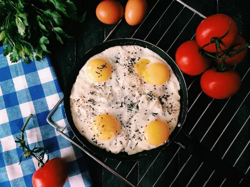 Яичница из четырех яиц с перцем на сковородке на решетке с помидорами рядом