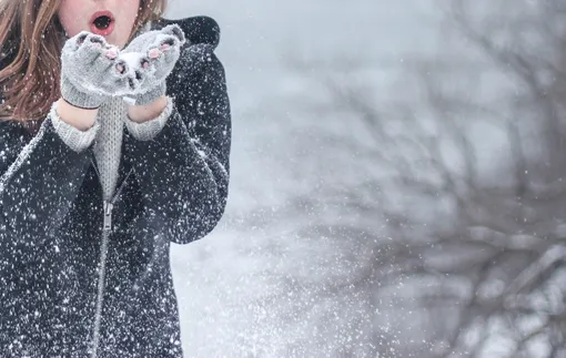 девушка сдувает с ладошней снежинки