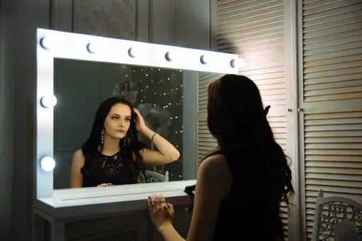 Девушка смотрит в зеркало и ищет признаки гормональных сбоев