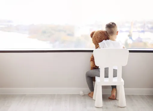 Ребёнок сидит у окна с игрушкой мишкой фото