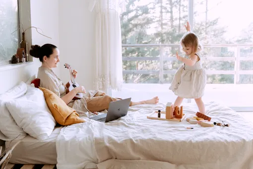 женщина играет на укулеле на кровати, а ребенок танцует