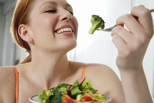 Девушка улыбается и ест брокколи, продукт против морщин и старения кожи