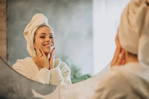 Девушка смотрит в зеркало в ванной