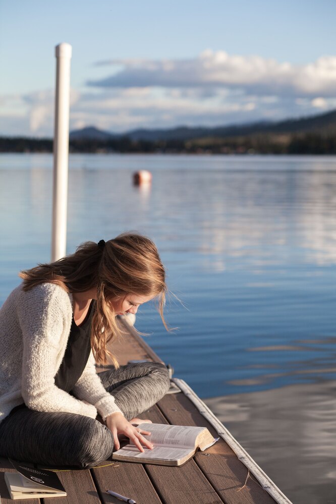 Девушка сидит около озера и читает книгу
