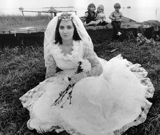 Невеста в свадебном платье сидит на берегу пруда