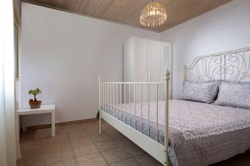 Классический стиль интерьера белой спальни с кованой кроватью, деревянным потолком, полом из керамической плитки