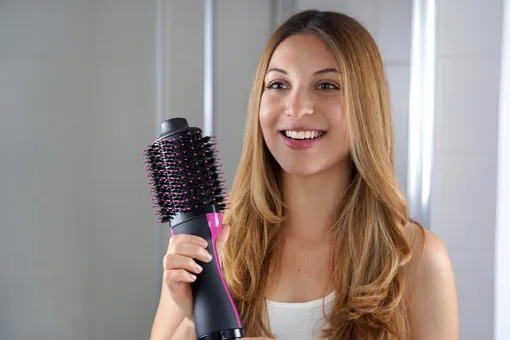 Улыбающаяся женщина держит электрическую расческу для волос