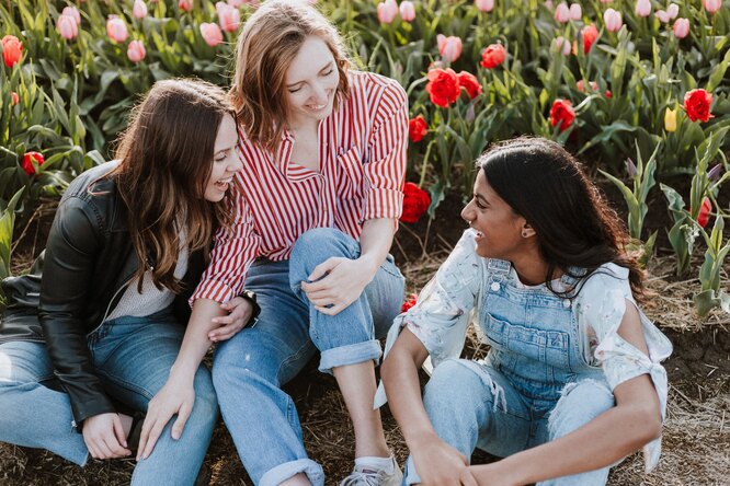Девушки сидят около клумбы с тюльпанами и смеются