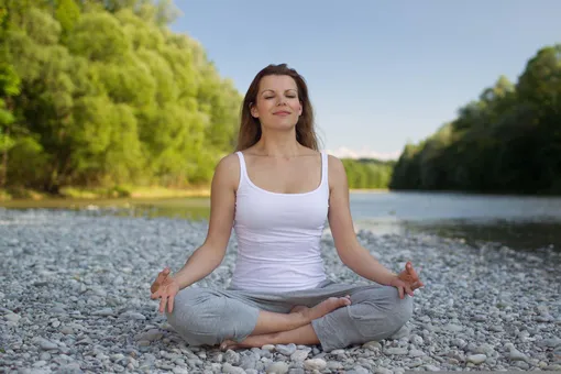женщина медитирует на камнях рядом с озером