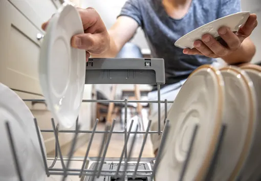 Мужчина кладёт тарелки в посудомоечную машину