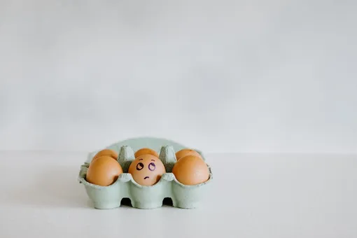 Яйцо с нарисованной рожицей в упаковке с яйцами