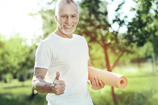 Позитивный мужчина с ковриком для йоги в руках показывает большой палец вверх