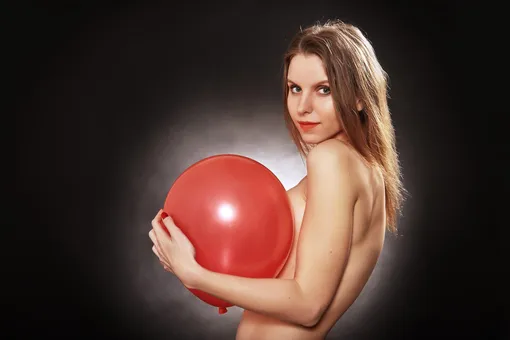Женщина держит красный воздушный шарик у груди