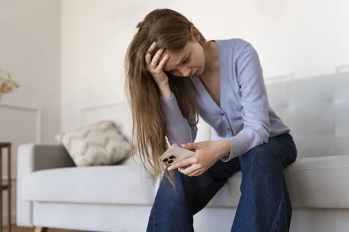 Расстроенная девушка держит в руках телефон