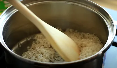 В большой кастрюле или сковороде разогрейте масло и добавьте промытый рис. Готовьте, постоянно помешивая, пока он не приобретёт золотистый оттенок. В процессе добавьте соль и тмин (кумин).
