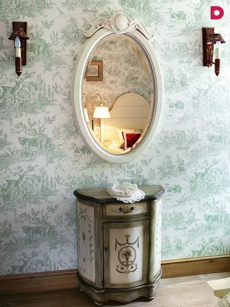 Фрагмент гостевой спальни с расписанным деревянным комодом и выбеленным зеркалом.