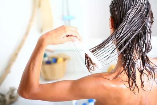 Женщина расчесывает волосы с нанесенной на них маской