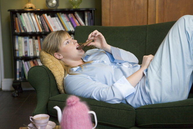 Женщина лежит на диване и ест шоколад, как перестать заедать стресс и одиночество