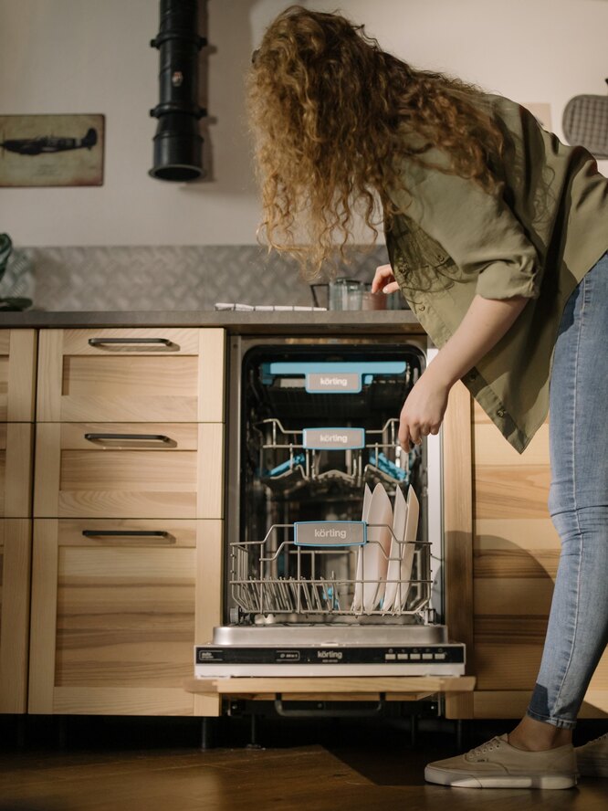 Девушка кладёт посуду в посудомоечную машину
