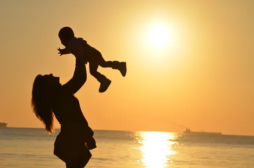 силуэт женщины с ребенком на руках на фоне закатного неба