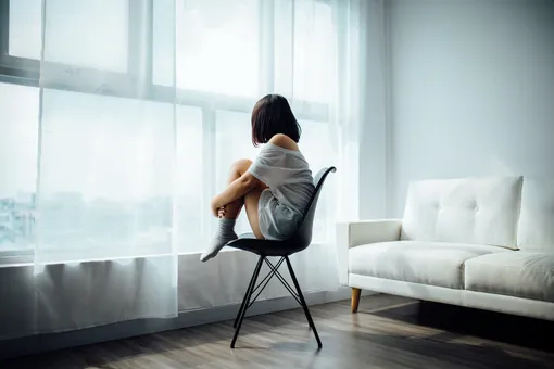 Девушка на стуле с ногами смотрит в окно, признаки гормональных нарушений