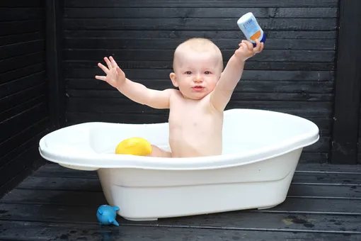 Малыш в ванночке держит в руках шампунь