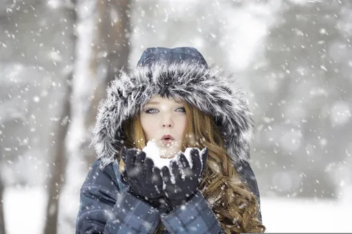 девушка в куртке сдувает снежинки со своих ладоней