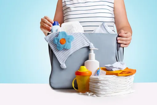 Мама складывает подгузники и вещи для младенца в сумку для подгузников