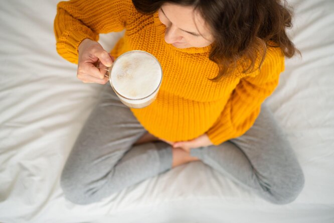 Беременная в желтом свитере с чашкой кофе с молоком