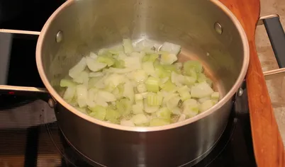 Для супа луковицу очистите, нарежьте кубиками. Стебель сельдерея измельчите. В тяжелой кастрюле разогрейте растительное масло и обжарьте лук до прозрачности. Добавьте в кастрюлю с луком сельдерей, перемешайте и обжаривайте 2-3 минуты на медленном огне. Влейте 1 литр воды и доведите до кипения.