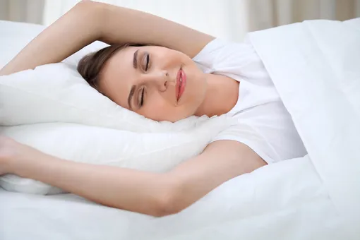 Девушка в белой футболке просыпается в кровати с белым постельным бельем, с добрым утром