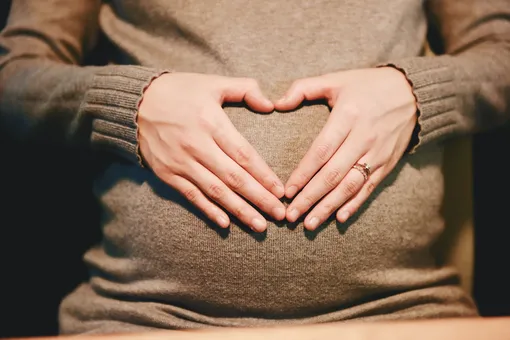 беременная девушка сложила сердечко из пальцев на животе