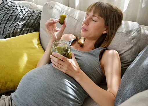 беременная женщина ест соленые огурцы из банки