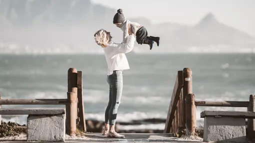 женщина держит на руках ребенка, стоя на берегу моря