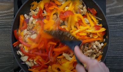 В глубокой сковороде разогрейте масло, добавьте нарезанные зелёный и красный перец, лук и курицу. Обжаривайте около 10 минут.