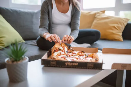 беременная женщина сидит по-турецки и берет из коробки пиццу