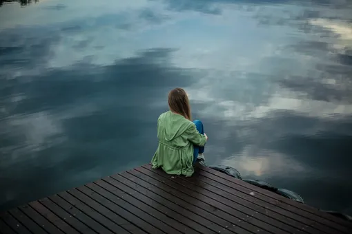 Девушка сидит одна около озера, высокая функциональная тревожность