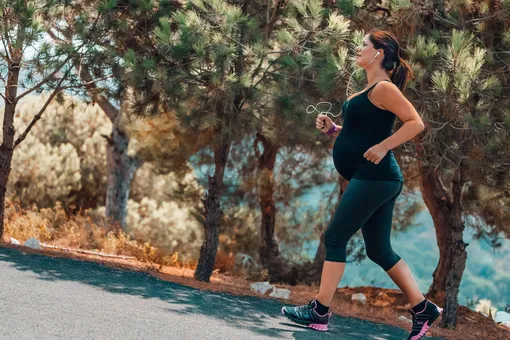 Беременная женщина бежит по дороге вдоль красивых сосен